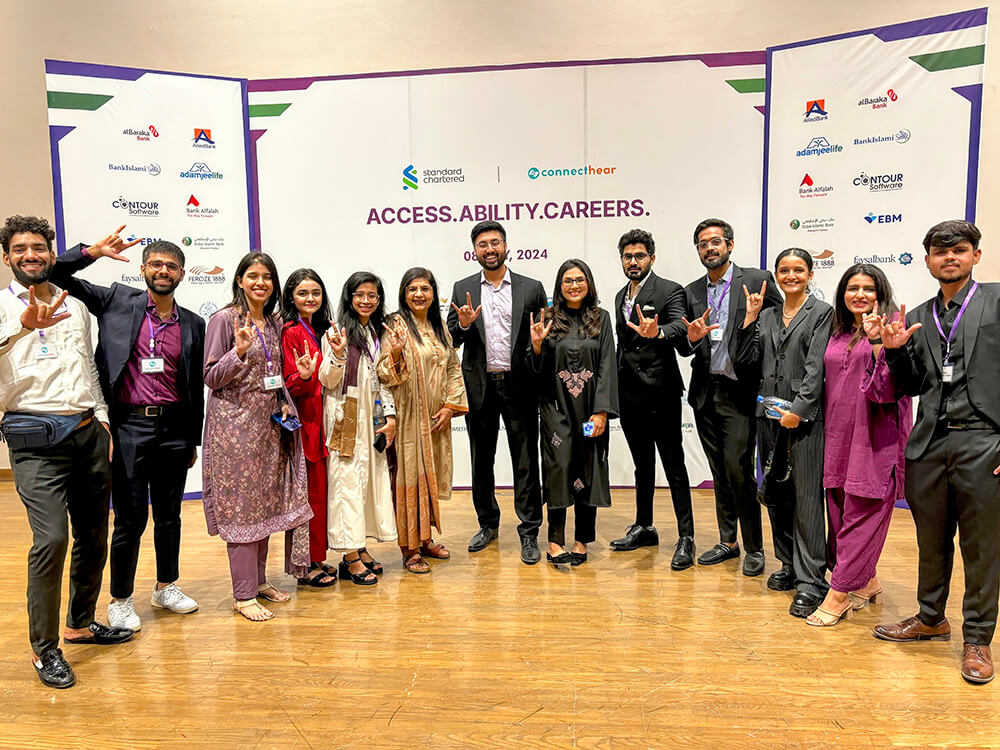 Azima Dhanjee, co-founder of ConnectHear, smiling while using sign language symbolizing communication, inclusion, and empowerment.